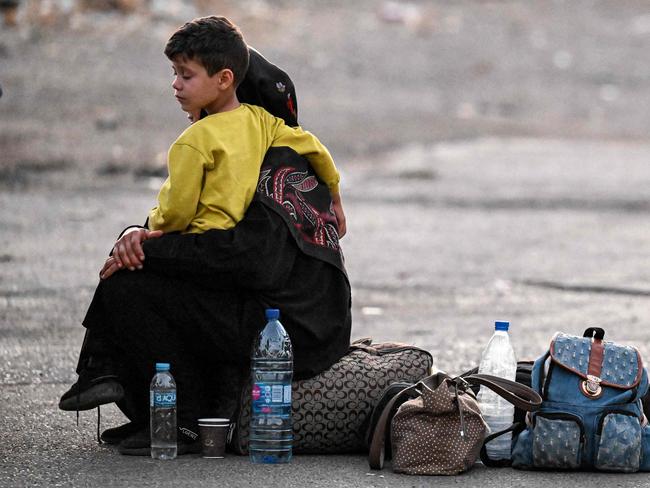 A woman sits with a child on her lap next to bags on the ground as people fleeing from Lebanon arrive on the Syrian side of the border. Picture: AFP.