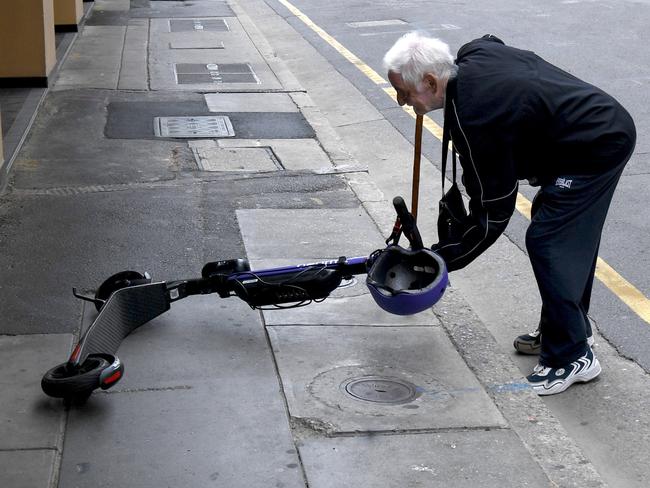 eScooters and eBikes city hazard. John Mete 80 from Victoria, tries to pick up an eScooter that was blocking the footpath pushing him on the road. The ebike was too heavy for him and when the eScooter alarm went off so he stopped moving it. Picture: Tricia Watkinson