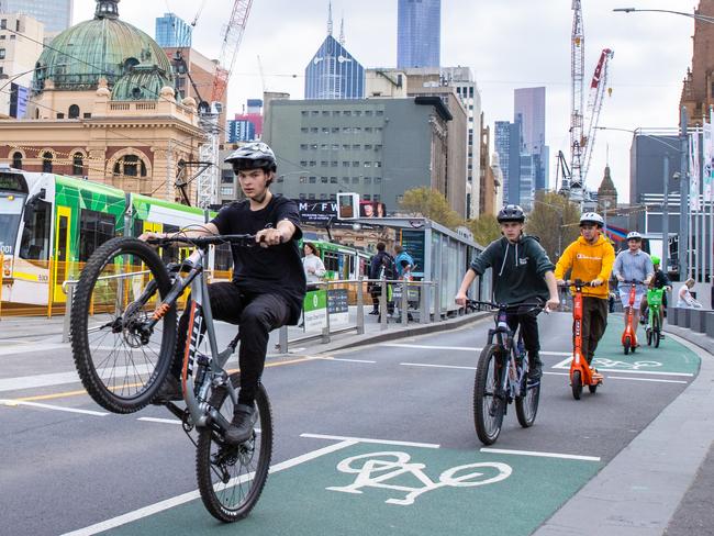 A boy riding a bicycle pops a mono riding in a bike lane with Melbourne skyline and landmarks federation square. Picture: Jason Edwards