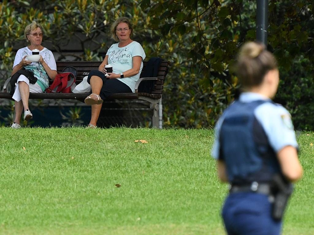 Two women sit on a bench as NSW Police officers patrol at Rushcutters Bay park in Sydney. Picture: Joel Carrett/AAP