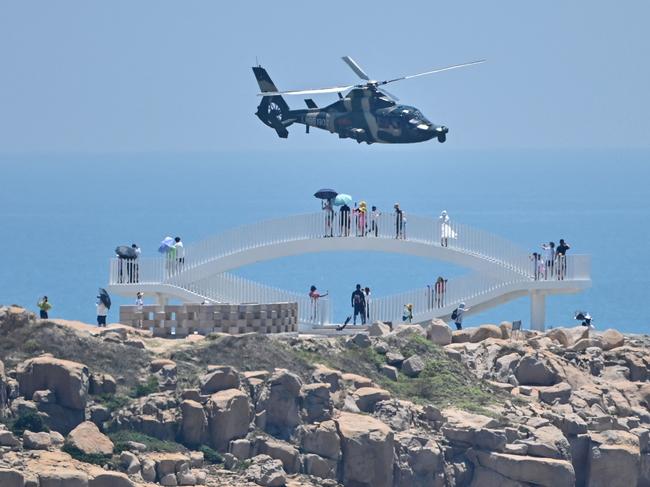 Tourists look on as a Chinese military helicopter flies past Pingtan island, one of mainland China's closest point from Taiwan. Picture: AFP