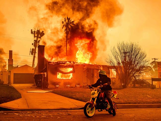 A motorcyclist stops to look at a burning home during the Eaton fire in the Altadena area of Los Angeles county, California. Picture: AFP