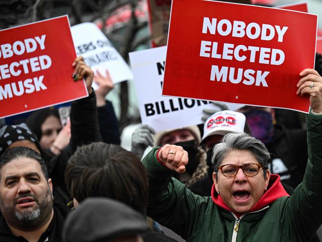 People hold up signs as they protest against US President Donald Trump and Elon Musk's "Department of Government Efficiency" (DOGE) outside of the US Department of Labor near the US Capitol in Washington, DC, February 5, 2025. Elon Musk has begun swinging his wrecking ball at the US government, with concerns growing over the unprecedented power that President Donald Trump has handed to the world's richest man. (Photo by Drew ANGERER / AFP)