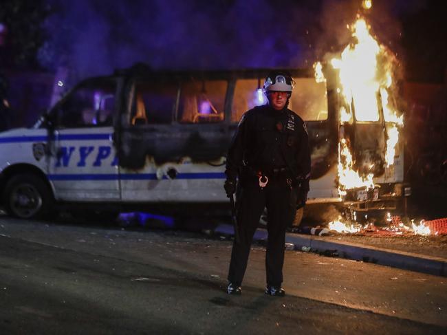 A police officer watches a crowd as a police vehicle burns near Fort Greene Park in the Brooklyn borough of New York. Picture: AP