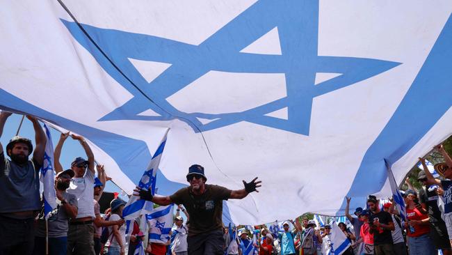 Anti-government protesters lift a large national flag during a demonstration near the Knesset. Picture: AFP.