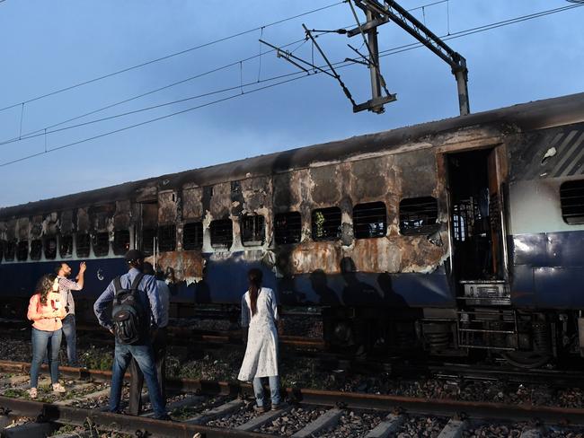 People stand next to a burned out train coach that had been set alight by supporters of a controversial guru, who had earlier been convicted of rape, at Anand Vihar railway station in New Delhi. Picture: AFP