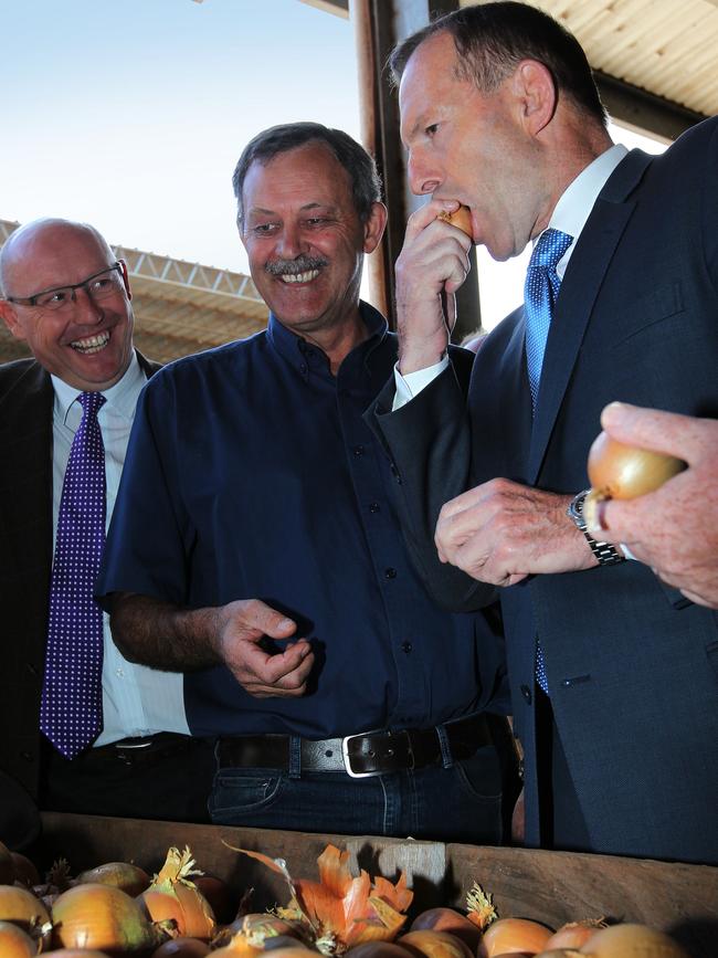 Former Lyons Liberal MP Eric Hutchinson, left, Charlton Farm Produce Director David Addison watch as Prime Minister Tony Abbott samples an onion during a visit to Charlton Farm Produce at Moriarty in 2015.