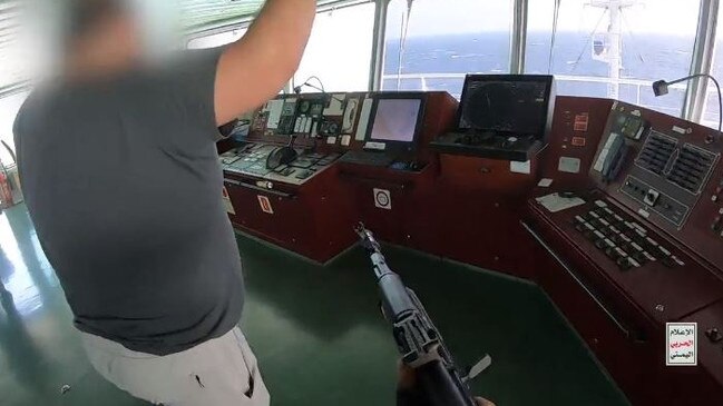 A crew member on the bridge is ordered to the controls of the ship at gunpoint.