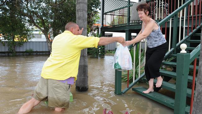 Keith Scanlan delivers vital supplies to his neighbour June Rowles at her home in George Street, Bundaberg, Queensland. Residents hold out, waiting for the flood tide to turn.