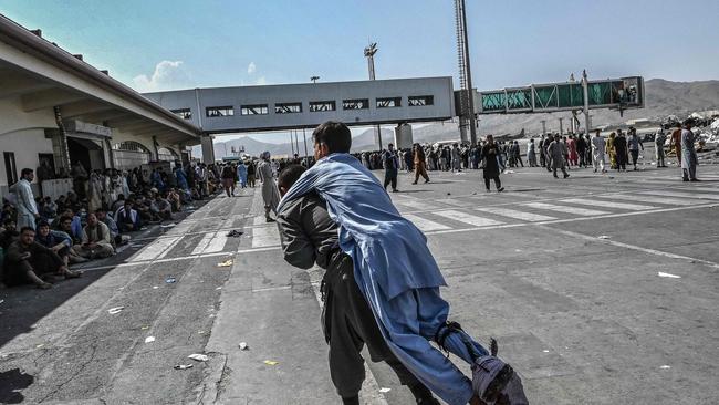 A volunteer carries an injured man as thousands rush to Kabul airport. Picture: Wakil Kohsar / AFP