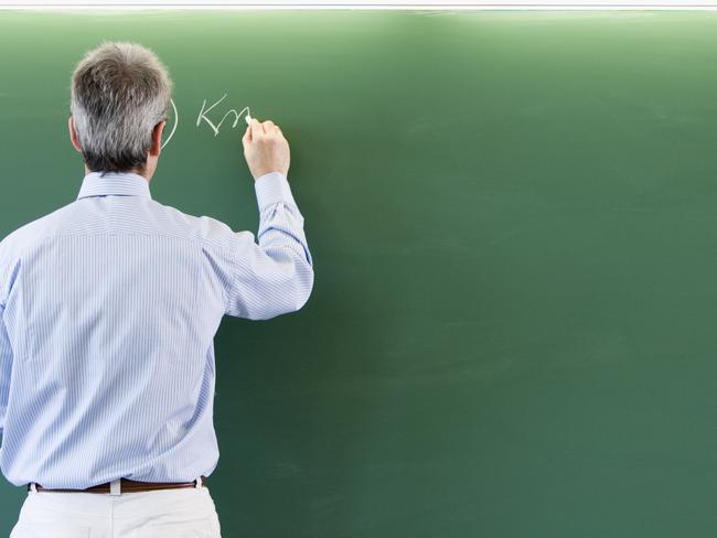 School teacher writing on green blackboard in front of empty classroom. Thinkstock.