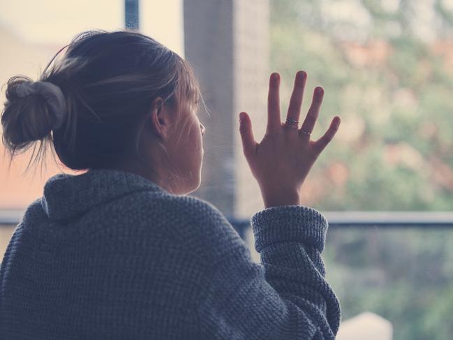 Portrait of a Woman looking through the window. She looks contemplative or sad lonely and depressed. She is holding her hand against the glass longing to go outside.