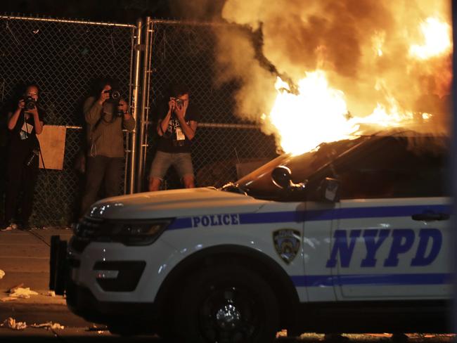 Photographers take pictures of a burning police car in the Brooklyn borough of New York. Picture: Seth Wenig