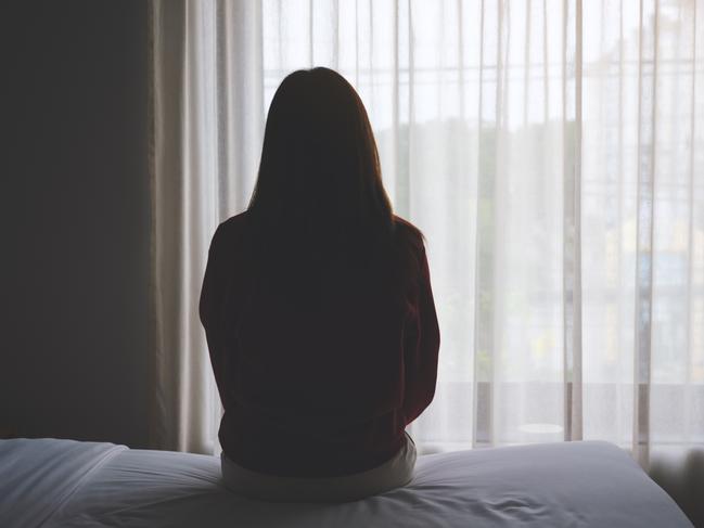 Rear view image of a woman sitting alone on a bed in bedroom