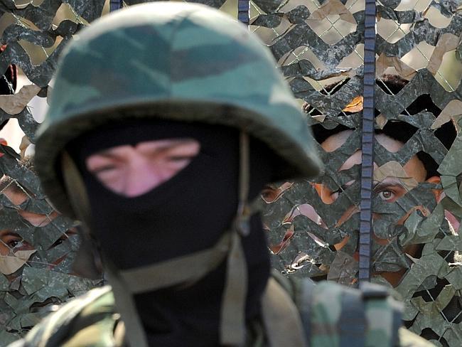 A Ukrainian soldier stands behind a fence while unidentified armed men block the headquarters of the Ukrainian Navy in Sevastopol.