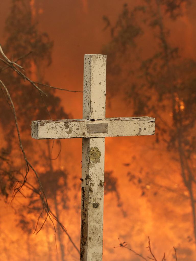 A bushfire burns behind a cross at Possum Brush, south of Taree. Picture: AAP