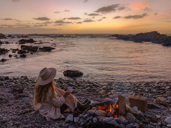 A visitor enjoys a wine by a camp fire on a King Island beach. Picture: Emilie Ristevski/Tourism Tasmania.