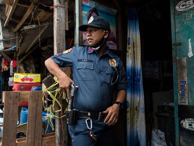 A police officer draws his gun as he prepares to enter the home of a suspected drug user in a Manila slum. Picture: Noel Celis