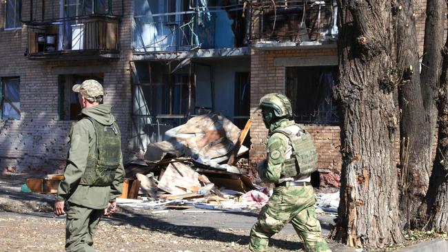 Local volunteers walk past a building damaged by Ukrainian strikes following its offensive into Russia's western Kursk region.