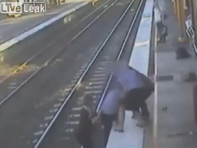 A passenger climbs down on to train tracks to help a man back to safety.