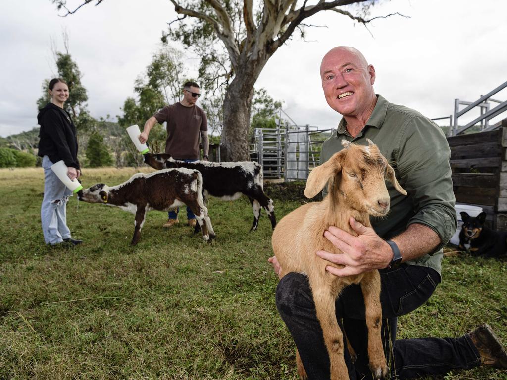 Traumatic brain injury survivor Jason Driscoll of Stones Throw Away with Fred the goat on his property near Pittsworth with homestay guests Lauren Stokes and Nick Overton feeding calves in the background, Saturday, March 29, 2025. Picture: Kevin Farmer