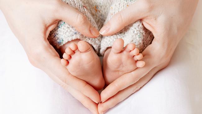 Baby feet in mother hands. Tiny Newborn Baby's feet on female Heart Shaped hands closeup. Mom and her Child. Happy Family concept. Beautiful conceptual image of Maternity