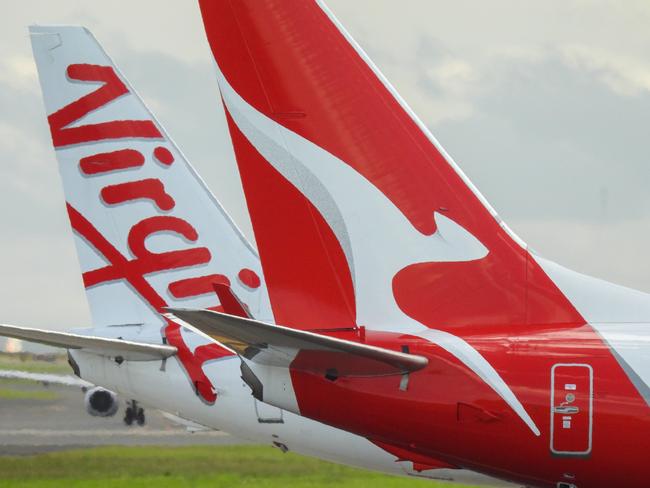 The vertical stabilisers of a Qantas Boeing B737-838 plane, registration VH-VZQ, and a Virgin Australia Boeing B737-8FE plane, registration VH-VUZ, waiting at the northern end of the main runway of Sydney Kingsford-Smith Airport in preparation for departure.  The Qantas plane is heading to Adelaide as flight QF741 and the Virgin plane is heading to Adelaide as flight VA428.  In the background is another Virgin B737-8FE plane. This image was taken from Nigel Love Bridge, Mascot on a sunny afternoon on 3 December 2023.