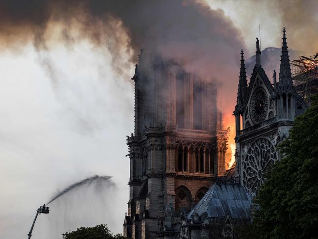 Firefighters douse flames billowing from the roof at Notre-Dame Cathedral in Paris on April 15, 2019. - A huge fire swept through the roof of the famed Notre-Dame Cathedral in central Paris on April 15, 2019, sending flames and huge clouds of grey smoke billowing into the sky. The flames and smoke plumed from the spire and roof of the gothic cathedral, visited by millions of people a year. A spokesman for the cathedral told AFP that the wooden structure supporting the roof was being gutted by the blaze. (Photo by THOMAS SAMSON / AFP)