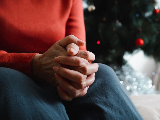 Lonely senior woman sitting at home in Christmas celebration. Close-up of an elderly woman's hand against background of decorated Christmas tree. Loneliness, sad holiday concept.