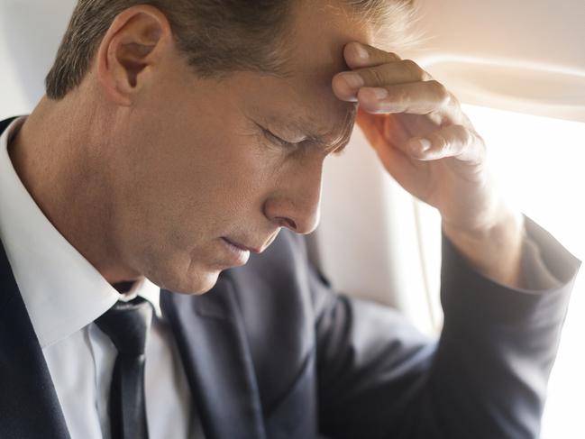 Feeling headache. Frustrated mature businessman touching his forehead with hand and keeping eyes closed while sitting at his seat in airplane