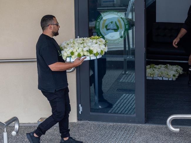 Loved ones carry floral arrangements into the mosque.