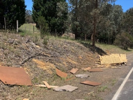 Pieces of a damaged fence lay dangerously along the side of a road.