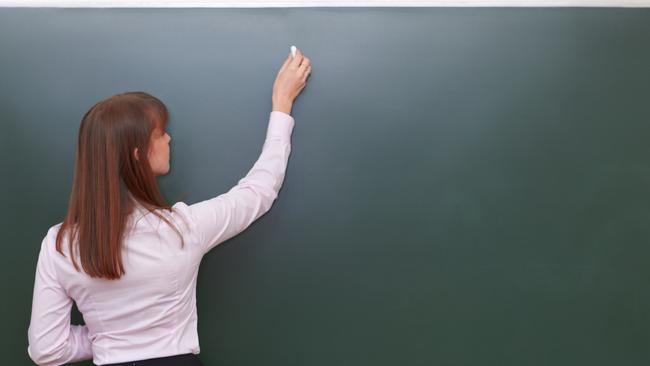 Teacher with chalk in front of chalkboard.