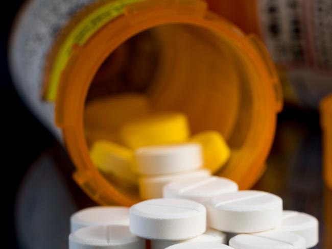 Oxycodone is the generic name for a range of opoid pain killing tablets. Prescription bottle for Oxycodone tablets and pills on glass table with reflections