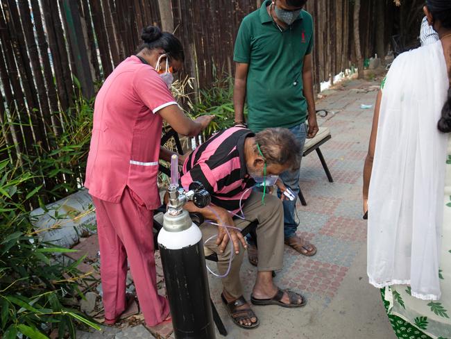 BENGALURU, INDIA - MAY 08: A nurse pats the back of Subramanya P, 60, struggling to breathe with the aid of supplemental oxygen provided by an NGO on a pedestrian pavement on May 08, 2021 in Bengaluru, India. India broke a fresh record on Thursday with over 412,000 new cases of Covid-19 as the total number of those infected according to Health Ministry data neared 20 million. The real figure could be up to ten times higher, many health experts say, due to a lack of widespread testing or reporting, and only patients who succumbed in hospitals being counted. Hospitals have begun turning away people suffering from Covid-19, having run out of space for the crushing number of people seeking help. (Photo by Abhishek Chinnappa/Getty Images)