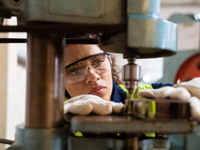 Close-up of female apprentice using yoke machine. Female engineer is wearing protective glasses in factory. She is working in manufacturing industry.