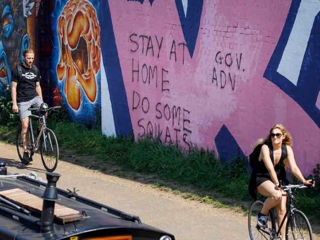 Cyclists ride past graffiti advising people to stay at home in east London due to the novel coronavirus COVID-19 pandemic. Picture: AFP