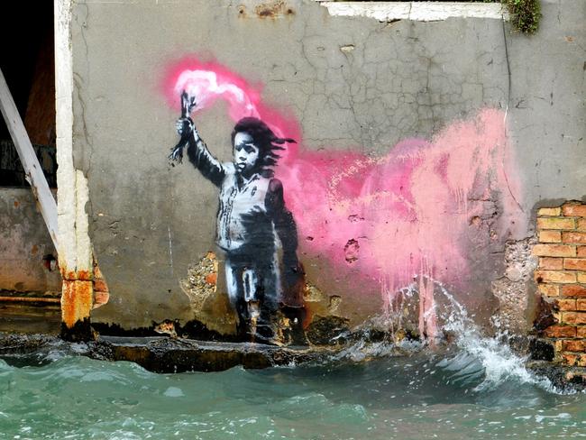 An alleged work by British street artist Banksy depicting a migrant child wearing a lifejacket holding a pink flare, is painted on the outer wall of a house overlooking the canal Rio de Ca Foscari, in Venice, on May 21, 2019. (Photo by Marco SABADIN / AFP) / RESTRICTED TO EDITORIAL USE - MANDATORY MENTION OF THE ARTIST UPON PUBLICATION - TO ILLUSTRATE THE EVENT AS SPECIFIED IN THE CAPTION