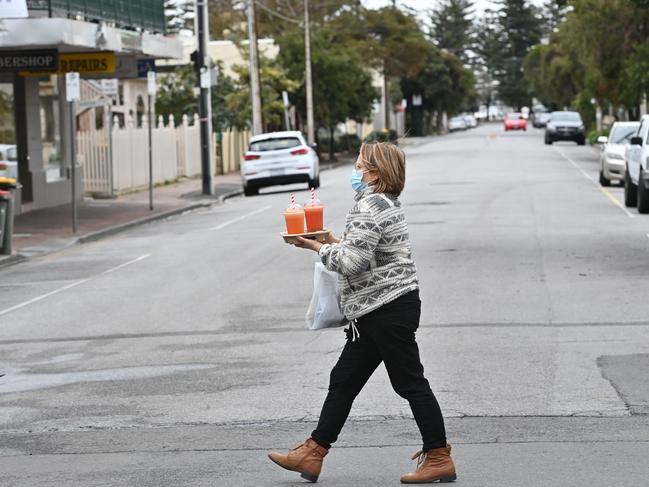 A woman carries drinks in a quiet, largely lifeless Glenelg on Thursday afternoon. Picture: Keryn Stevens.