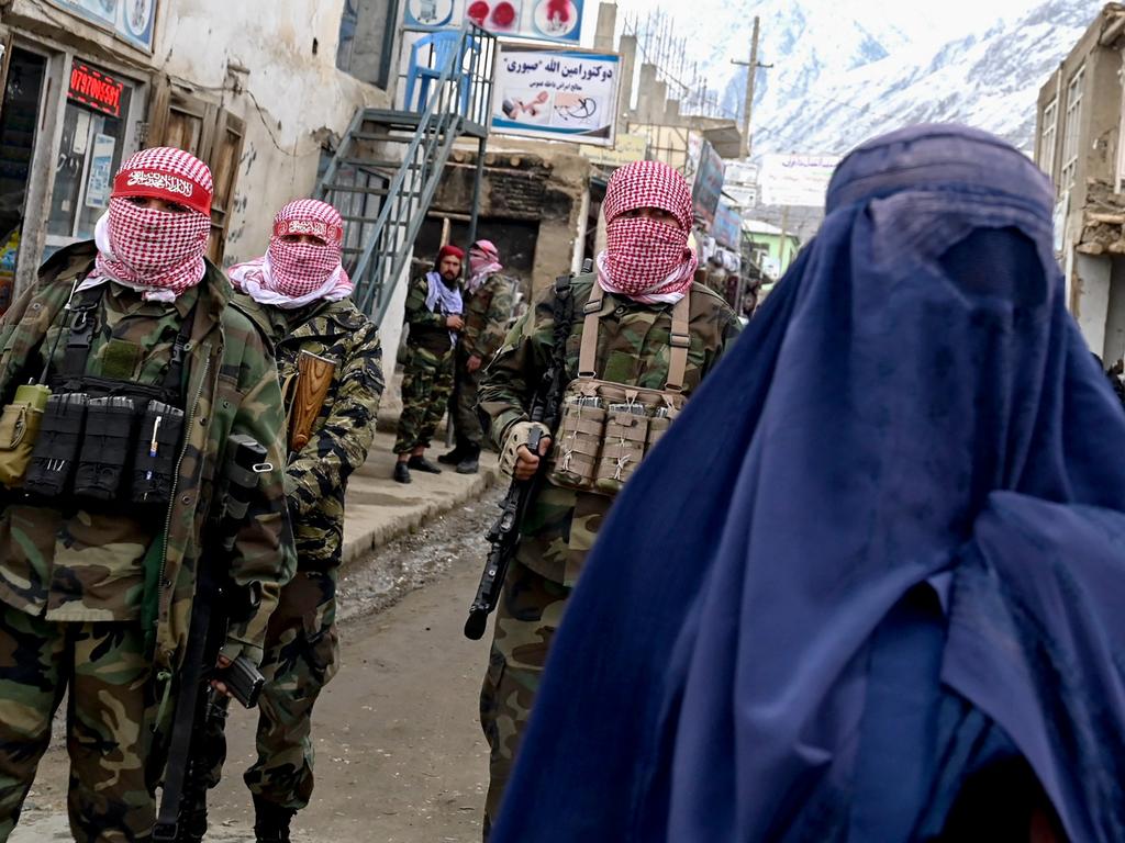 Taliban security personnel stand guard as an Afghan burqa-clad woman walks along a street at a market in the Baharak district of Badakhshan province. Picture: AFP