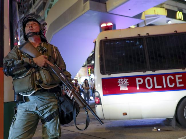 A police officer armed with a shotgun looks up at protesters on a bridge. Picture: AP