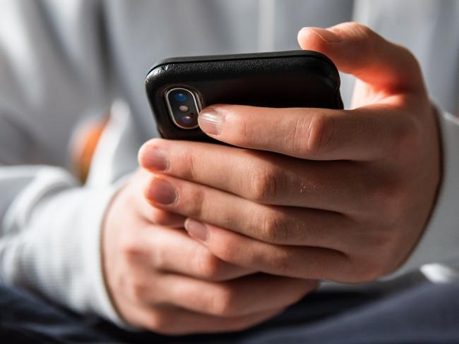 Stock image of Close up of hands of teen boy in white sweater texting on phone.Credit >Getty