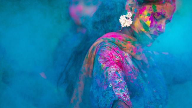 Young woman dancing around blue powder while celebrating the Indian Holi Day