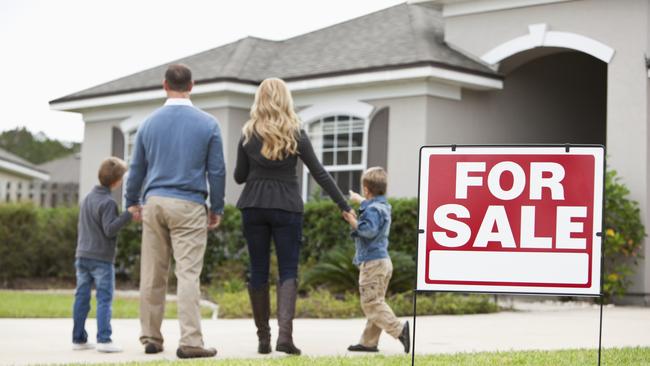 Family with two boys (4 and 6 years) standing in front of house with FOR SALE sign in front yard.  Focus on sign.