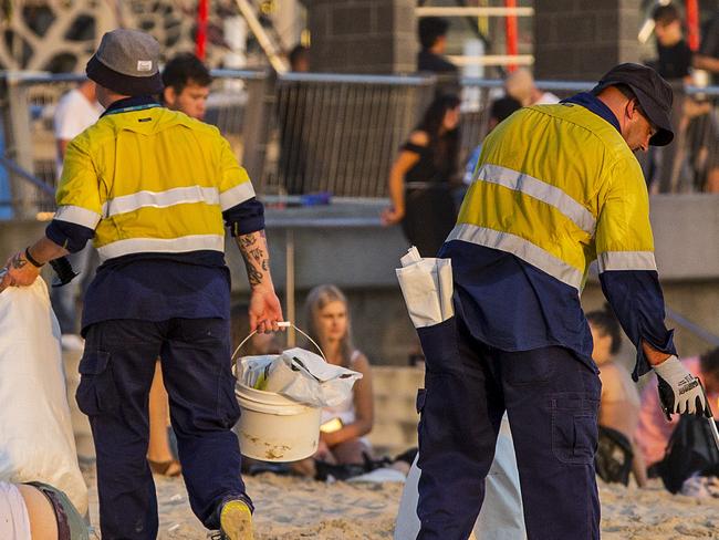 Two council workers cleaning rubbish of the beach as a man lays asleep next to them  on the first day of 2017 at Surfers Paradise.  Picture: Jerad Williams