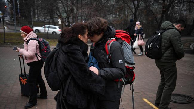 People hug as a woman with a suitcase passes by outside a metro station in Kyiv in the morning of February 24.