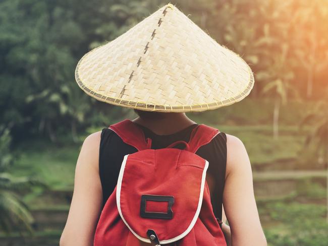 Young lady with traditional Asian hat and backpack standing and looking at tea plants (intentional sun glare)