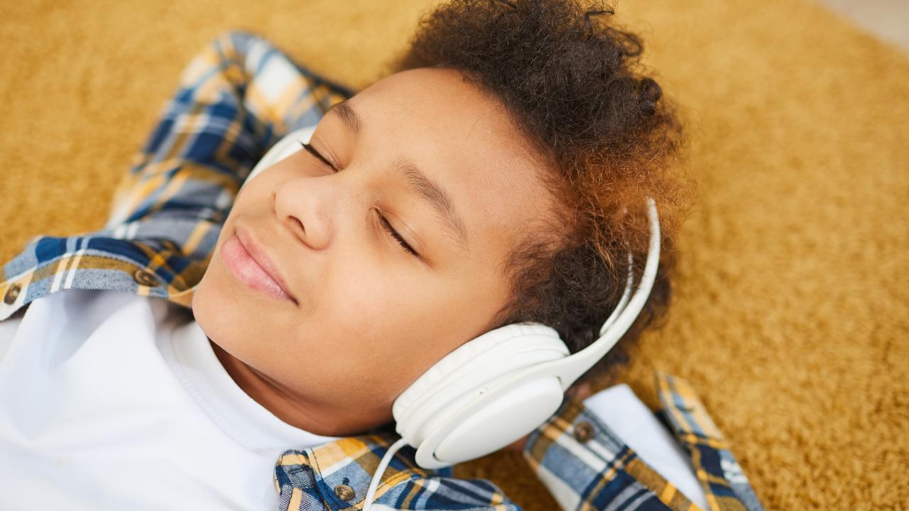 Portrait of teenage African boy wearing headphones and lying on floor while enjoying music with eyes closed, copy space