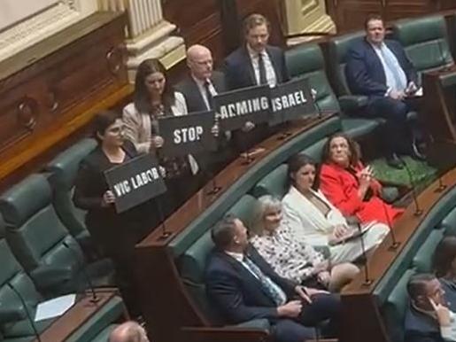 Greens MPs holding up signs which read: 'Vic Labor stop arming Israel'.