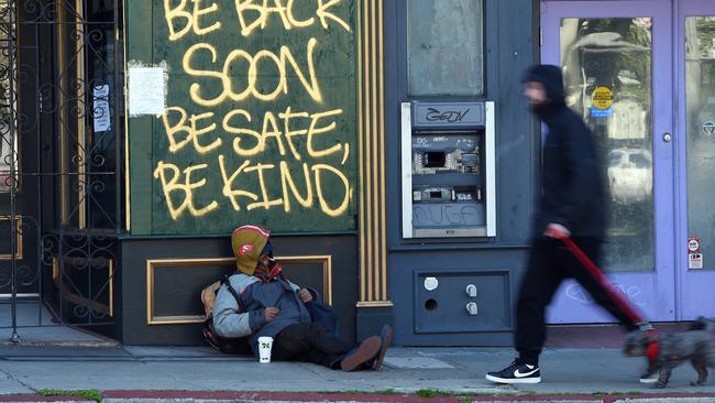 A man walks his dog past a homeless man sleeping under a message painted on a boarded up shop in San Francisco. Picture: AFP